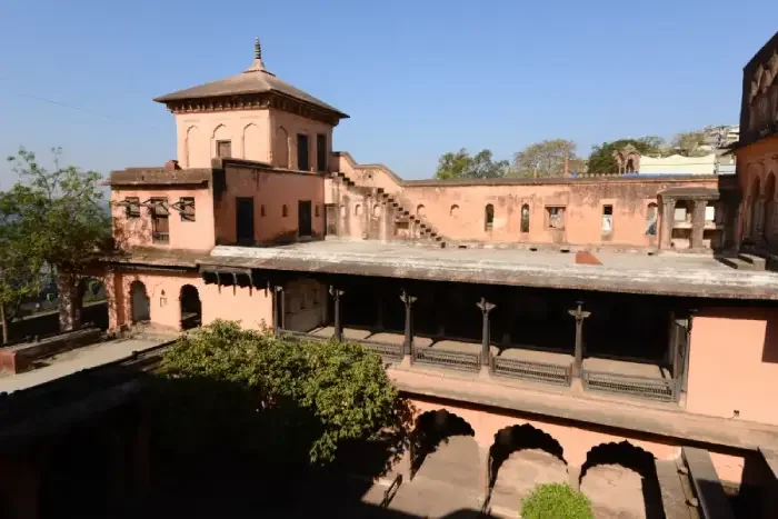 गौहर महल का खुला आँगन, उसके चारों ओर मेहराबों और लकड़ी के खंभों वाले बरामदे तथा ऊपर गुलाबी रंग की इमारत।