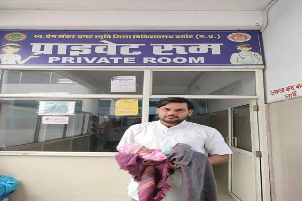 दमोह जिला अस्पताल के प्राइवेट रूम के बाहर कपड़े में लिपटे नवजात को गोद में लिए खड़ा एक व्यक्ति