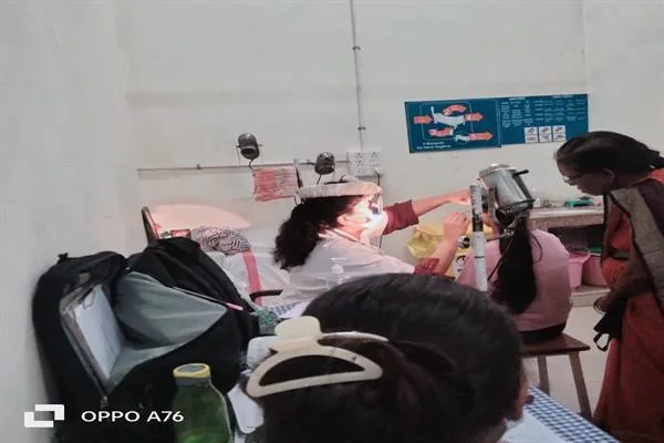 स्वास्थ्य केंद्र के कमरे में एक चिकित्साकर्मी उपकरण के पास बैठी बच्ची की जांच करते हुए, आसपास अन्य महिलाएं मौजूद हैं